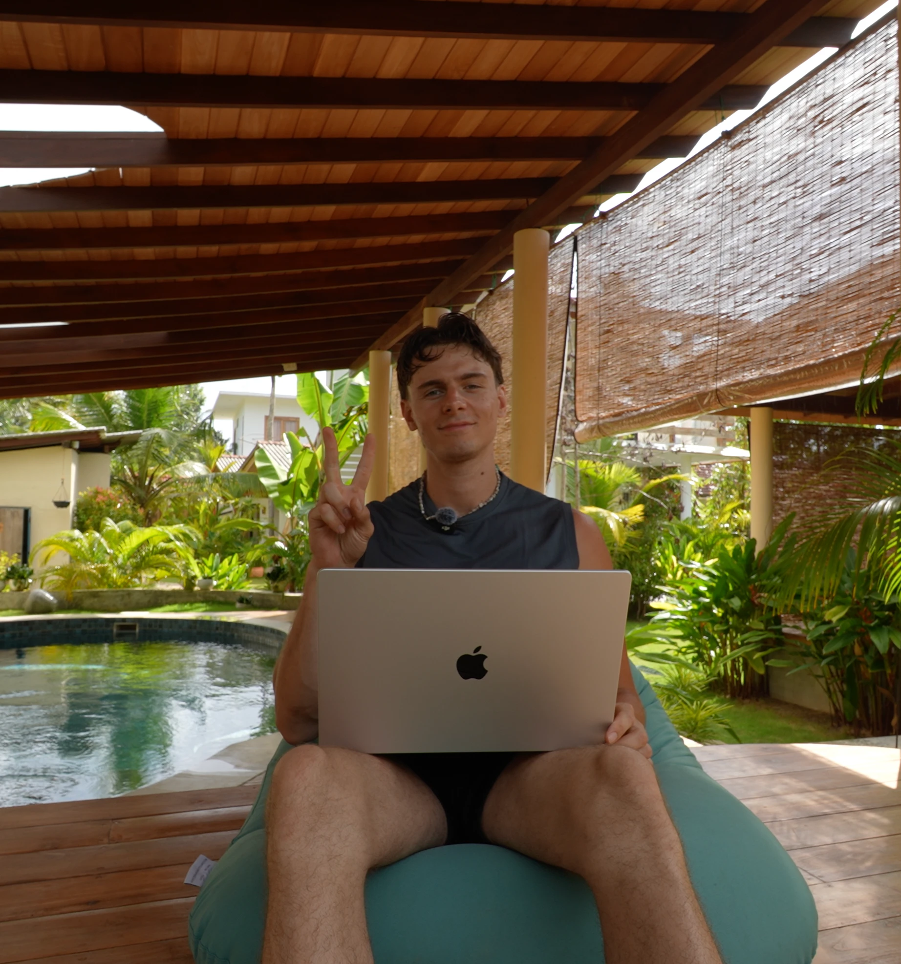 Odin at a pool, MacBook in one hand, peace sign with the other